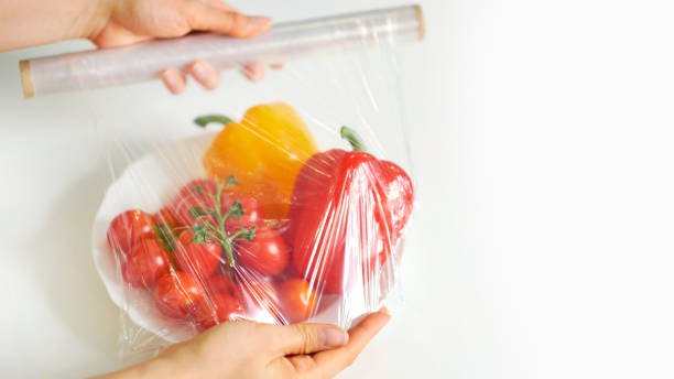 Woman using food film for food storage on a white table. Roll of transparent polyethylene food film.