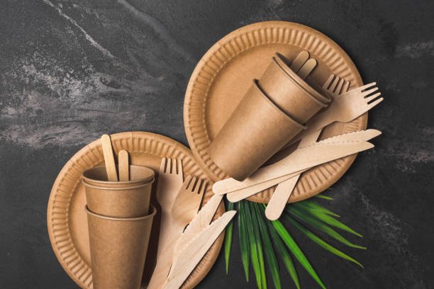 Top view of brown craft disposable take-out cup, plate, and wooden fork, knife for picnic on black marble background