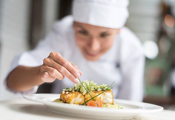 Cook decorating a plate and putting the ultimate touches - focus on foreground